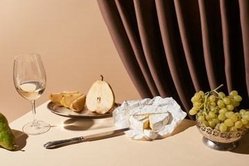 classic still life with pears, grape, white wine and Camembert cheese on table near curtain isolated on beige