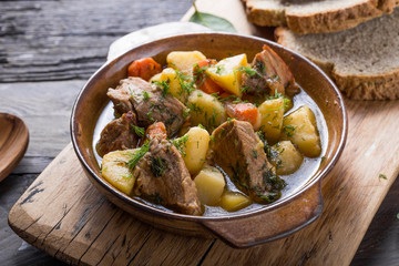 Irish dinner. Beef meat stewed with potatoes, carrots and soda bread on wooden background, top view, copy space. Homemade winter comfort food - slow cooked