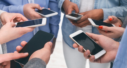 Closeup of diverse people standing in circle holding smartphones