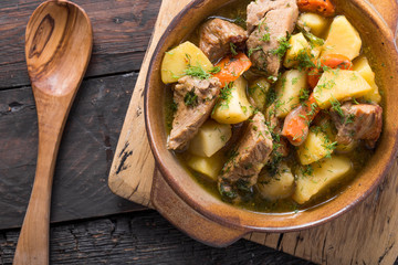Irish dinner. Beef meat stewed with potatoes, carrots and soda bread on wooden background, top view, copy space. Homemade winter comfort food - slow cooked