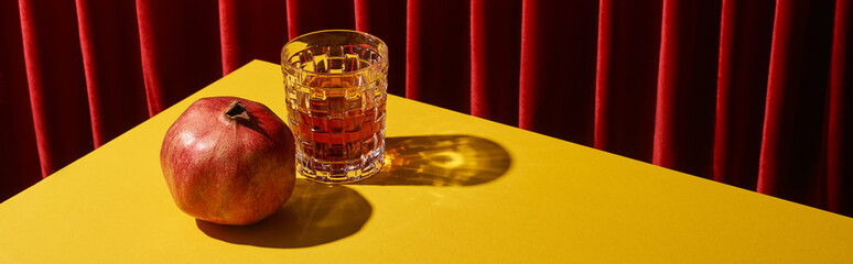 classic still life with pomegranate near glass of red wine on yellow table near red curtain, panoramic shot © LIGHTFIELD STUDIOS