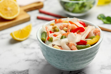 Tasty cooked rice noodles with shrimps and vegetables on white marble table