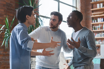 Emotional young guys having quarrel at office