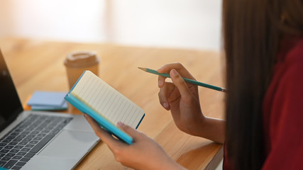 Side shot of young writer woman is writing/giving concentrate on notebook while sitting at the wooden table.