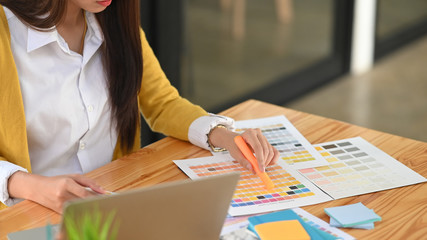 Close-up image of beautiful designer choosing the color from color guide while sitting at the wooden working desk.