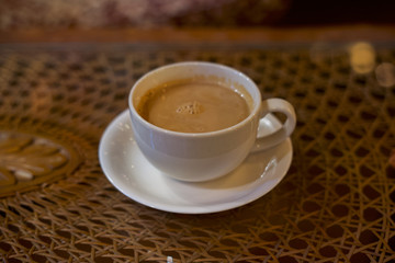 Coffee in white cup on wooden table in cafe with lighting background