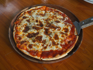 Top view of sliced thin-crusted Italian Margherita pizza on a wooden serving plate on a table.