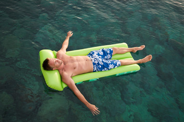 Overhead full length view of man relaxing on a green inflatable lilo floating on the water