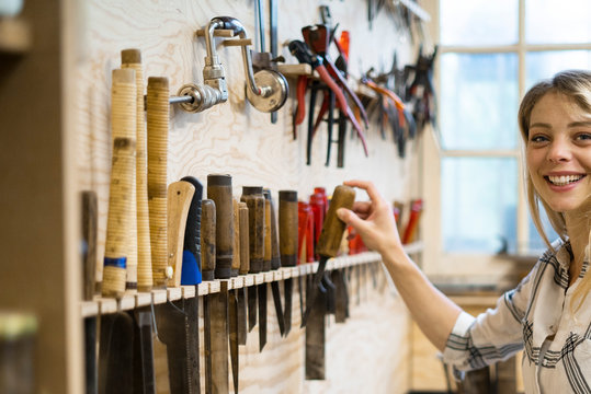 Portrait of smiling young woman holding hand tool in workshop