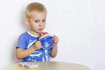 Blonde Toddler boy drinking water from a drinker with a straw