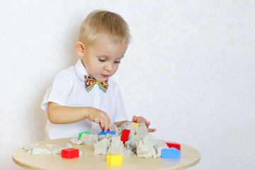 A 2-year-old toddler boy is playing with kinetic sand and colorful shapes, this activity develops fine motor skills in kindergarten children 