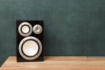 Single modern black audio speaker in interior on wooden desk near the wall