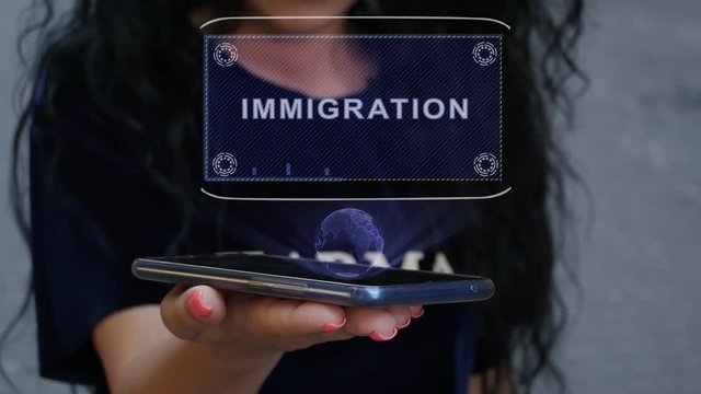 Unrecognizable curly brunette woman showing HUD hologram with text Immigration. Girl uses technology of the future on a mobile screen