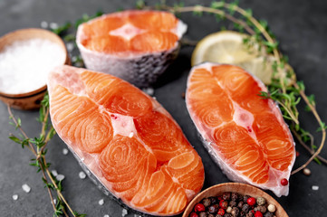 fresh raw salmon steaks on a stone background with salt, pepper, lemon 