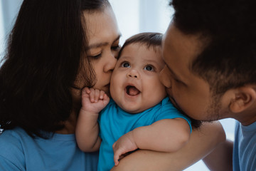 baby boy smiles when kissed by father and mother while joking