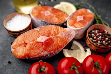 fresh raw salmon steaks on a stone background with salt, pepper, tomatoes, lemon