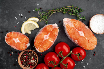 fresh raw salmon steaks on a stone background with salt, pepper, tomatoes, lemon