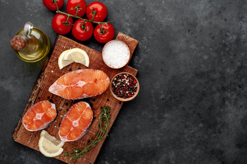 fresh raw salmon steaks on a stone background with salt, pepper, tomatoes, lemon with copy space for your text