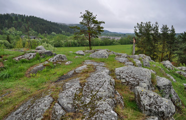 Rocky hills in the middle of meadows, against the backdrop of wooded hills on a spring foggy day