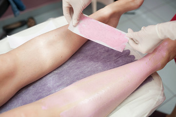 beautician removes hair on the legs with a wax strip