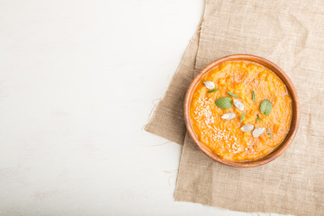 Sweet potato or batata cream soup with sesame seeds in a wooden bowl on a white wooden background. top view, copy space.