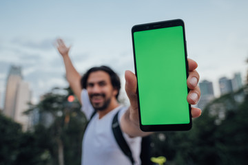 A man holds a phone with a green screen and stands against the backdrop of a metropolis