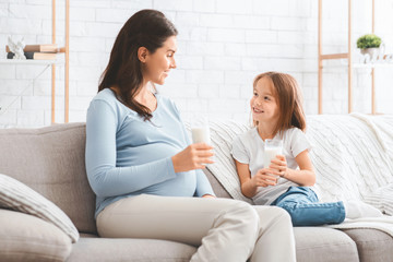 Pregnant loving mom drinking milk with her sweet daughter