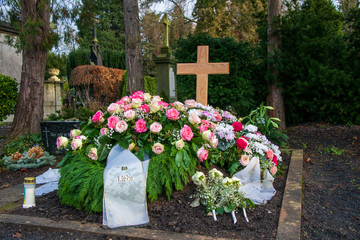 Viele bunte Kränze mit Schleifen auf einem Grab