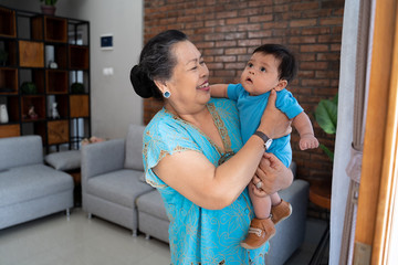 Fototapeta na wymiar Grandma stand with carrying little grandson wearing casual clothes at home