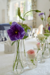 Beautiful floral arrangement on wedding table in restaurant, copy space. Bouquet of pink roses, purple eustoma and greenery in glass vases. Luxury wedding decorations