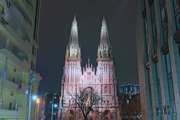 Obraz premium Picturesque view of illuminated ancient Saint Nicholas Roman Catholic Cathedral (House of Organ Music). View of the cathedral between the high-rise buildings. Kyiv, Ukraine