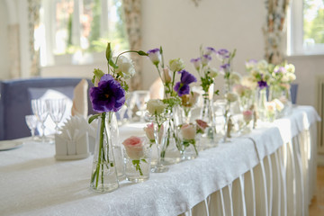 Beautiful floral arrangement on wedding table in restaurant, copy space. Bouquet of pink roses, purple eustoma and greenery in glass vases. Luxury wedding decorations