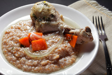 barley porridge with stewed chicken leg on a white plate, close-up