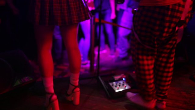 Close-up photo of young hipster woman legs and red guitar in neon lights. Rock musician is playing electrical guitar.
