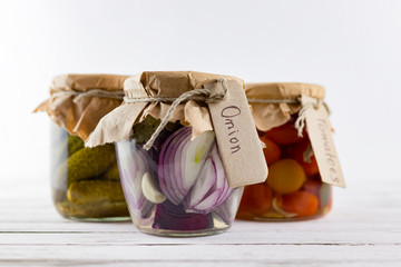 glass jars of fermented white cabbage, cucumbers, tomato, onions. vegetables on a light background. fermentation is a source of probiotic