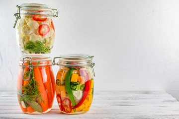 Fototapeta na wymiar three glass jars of fermented cauliflower,carrots, vegetables on a light background. fermentation is a source of probiotic. copy space