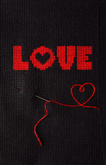 The word love is embroidered with red threads on black cloth.
