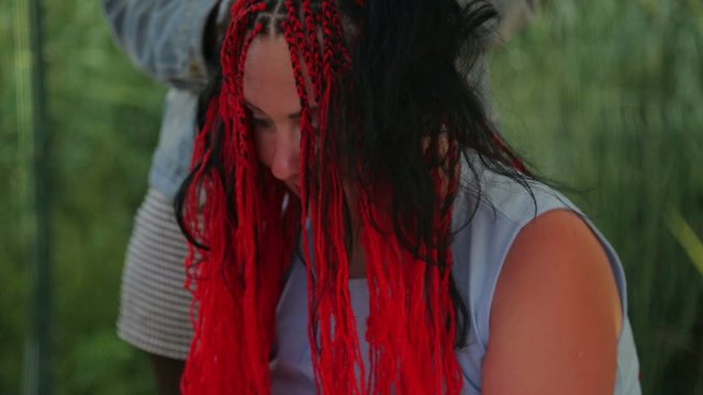 A young woman sits while a black hairstylist braids her braids.