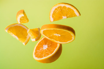 Bright green background, slices of orange are different sizes in air. Vitamin C. Healthy nutrition. Citrus.