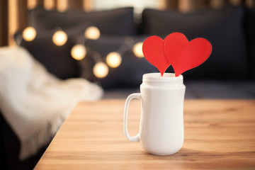 Valentines Day Red Heart Tags In White Mug  On The Coffee Table. Sofa In The Background. Red Heart Mock Up. Valentine Day Concept. Branding Mockup