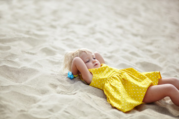 Adorable child in dress posing outdoors. Little baby girl relaxing by the sea. Kid resting at beach in summer. Concept of summer,childhood and leisure