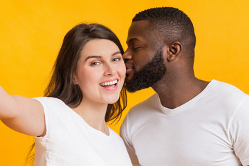 Fototapeta premium Romantic multiracial couple taking selfie, loving black guy kissing his girlfriend