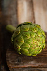 Fototapeta premium Fresh green artichoke on rustic wooden background. Minimalism. Concept of healthy and not boring vegetarian food. Close up, macro