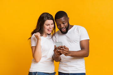 Surprised multiracial couple looking at smartphone screen and exclaiming with joy