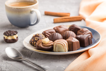Different chocolate candies and a cup of coffee on a gray concrete background. side view, selective focus.
