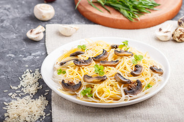 Rice noodles with champignons mushrooms, egg sauce and oregano on a black concrete background. side view, selective focus.