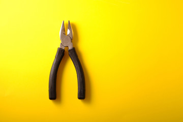 Pliers with black handles on a yellow background, top view