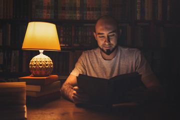 Reading and education. A man in the library reading a book in the evening by the light of a lamp....