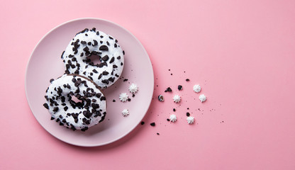 two delicious fresh hearty black and white donuts lie on a pink  plate on a pink background.