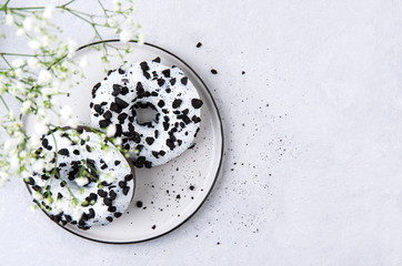 two delicious fresh hearty black and white donuts lie on a white  plate with flowers gypsophila on a white background.